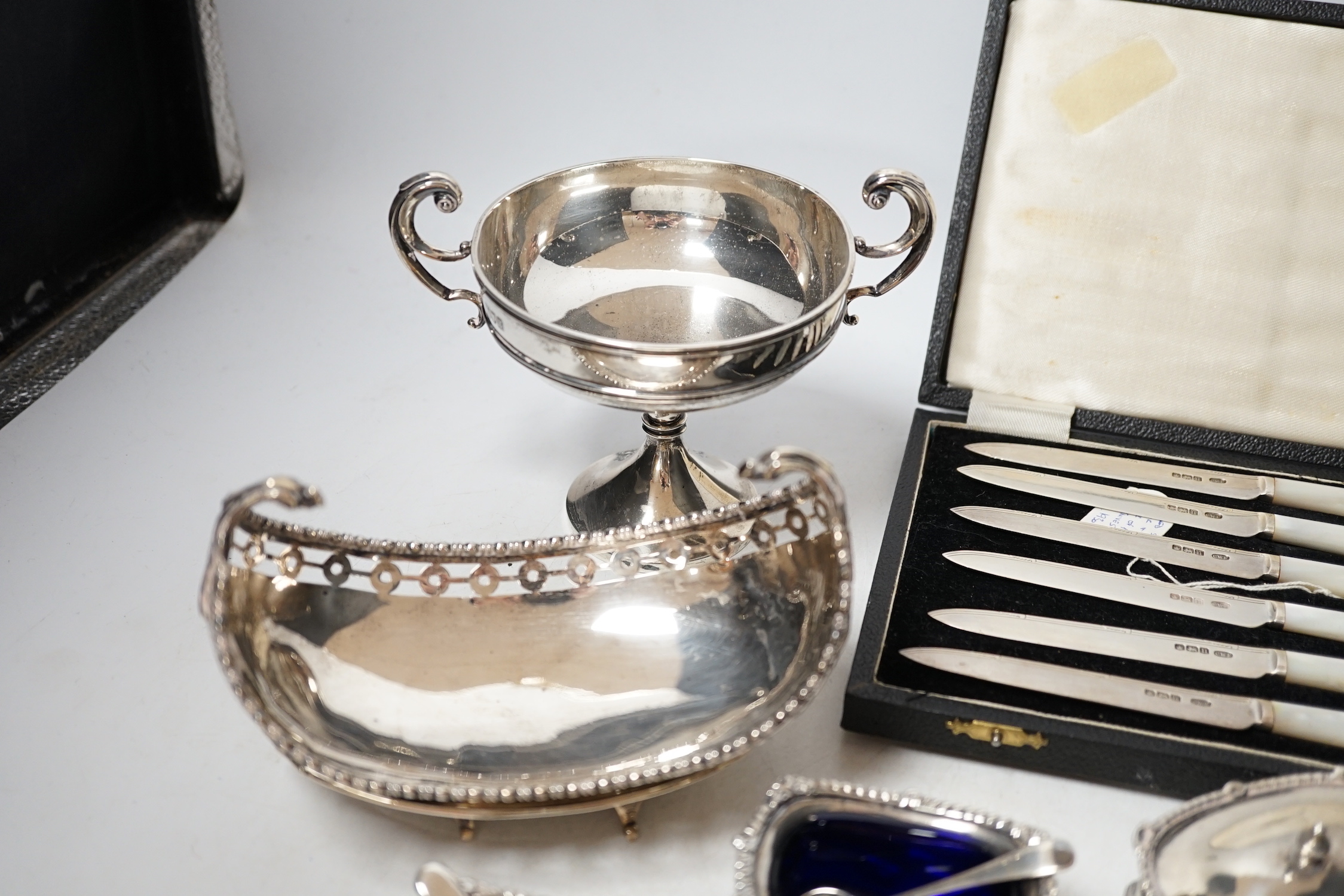 An Edwardian small silver two handled pedestal dish, London, 1902, height 12cm, a silver inkstand base, a silver boat shaped dish (lacking stand), a pair of silver salts with blue glass liners and spoons, three other sil